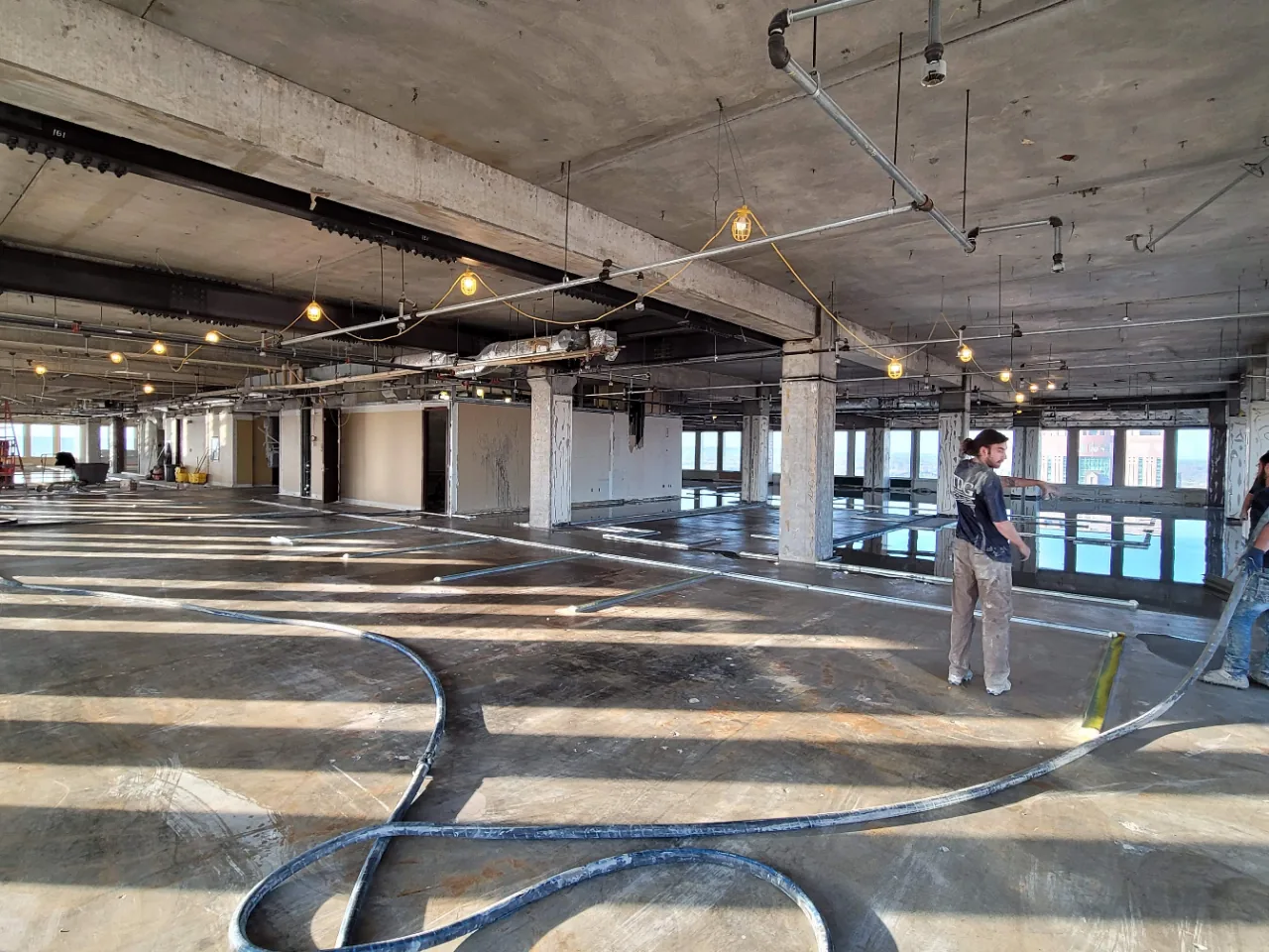 Open high-rise office floor at 500 West with the pump hose run out and metal screed rails laid across the slab before the pour