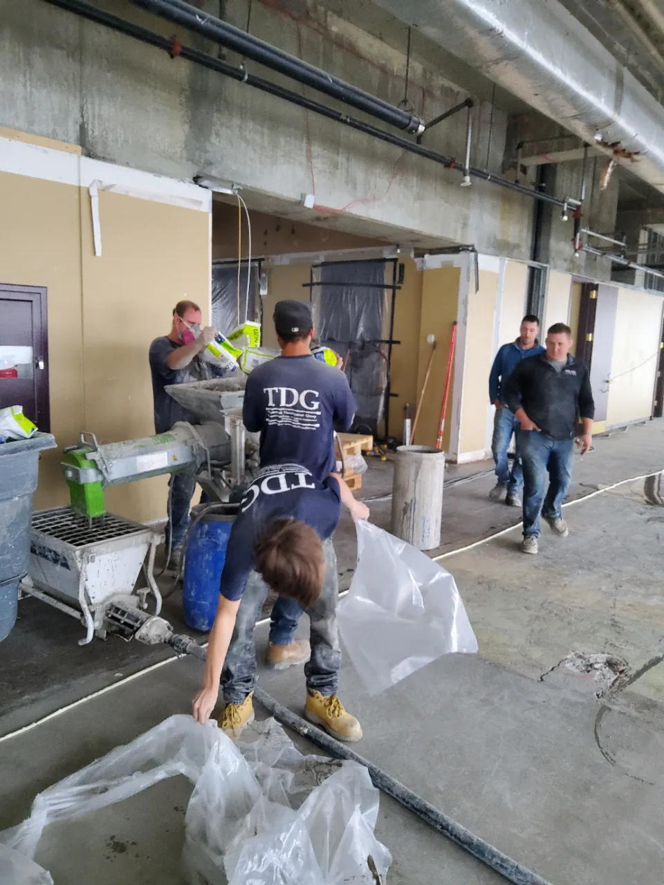 Installers in TDG shirts feeding bags into the pump hopper and clearing empties from the floor
