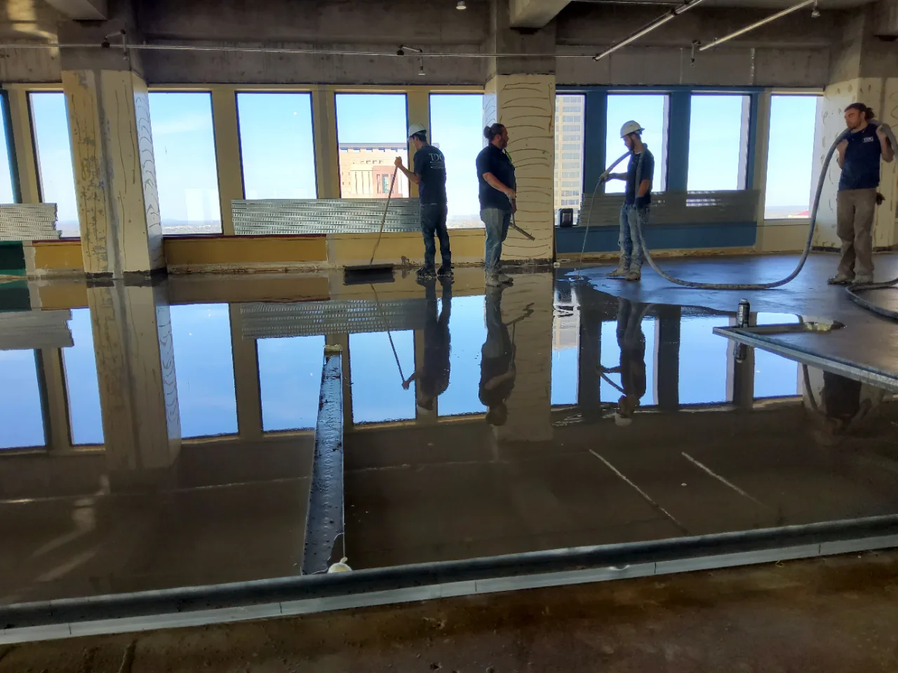 Freshly poured self-leveling underlayment reflecting the window wall and skyline like glass